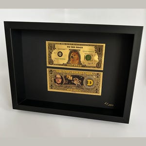 Peut inclure: Deux billets encadrés de couleur or avec le texte "DOG ECOIN RESERVE NOTE" et "TO THE MOON" imprimé dessus. Le billet du haut présente un chien Shiba Inu et le billet du bas présente un homme avec des lunettes. Les deux billets portent le texte "ONE DOGE" imprimé dessus. Le coin inférieur droit du cadre porte le texte "A1/100" imprimé dessus.