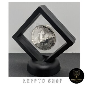 May include: A silver-colored Bitcoin coin is displayed in a black acrylic display case with a black base. The coin features the Bitcoin logo and the words "Digital Decentralized Peer to Peer."