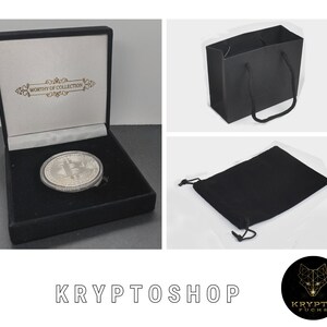 May include: A silver coin with a Bitcoin logo is displayed in a black velvet box with a white interior. The box has a gold inscription that reads "Worthy of Collection". The coin is also included in a black velvet pouch and a black paper shopping bag.