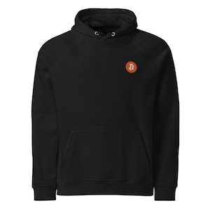 Könnte beinhalten: Schwarzer Kapuzenpullover mit Fronttasche und Kordelzugkapuze. Auf der Brust ist ein orangefarbenes Bitcoin-Logo aufgestickt. Das Sweatshirt ist aus einem weichen Material gefertigt.