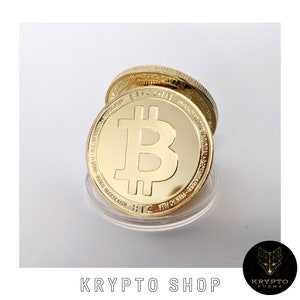 Może przedstawiać: Złota moneta Bitcoin z symbolem Bitcoina w środku. Moneta znajduje się w przezroczystym plastikowym pojemniku.