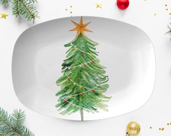 May include: White, oval-shaped serving platter with a watercolor Christmas tree design. The green tree is decorated with colorful lights and topped with a gold star. Festive holiday decor.