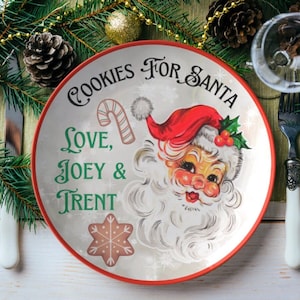 May include: A white ceramic plate with a red rim features a vintage illustration of Santa Claus with the text "Cookies for Santa Love, Joey & Trent".