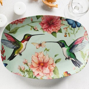 May include: Oval serving platter with a green background and floral design. Two hummingbirds are perched on branches, one with red and green feathers and the other with green and blue feathers.