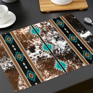May include: A rectangular placemat with a cowhide pattern and a Southwestern design. The placemat features a brown and white cowhide print with a central band of black, brown, and turquoise geometric patterns. A white cup and spoon are visible.