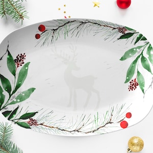 Puede incluir: Plato ovalado blanco para servir con un diseño de acuarela de ramas de pino verdes, bayas rojas y una silueta blanca de un reno.