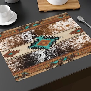 May include: A brown and white cowhide patterned placemat with a turquoise and brown geometric design. The placemat has a fringed edge.