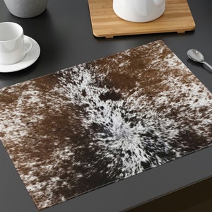 May include: Brown and white cowhide placemat with a swirling pattern. The placemat is made of a soft, textured material.