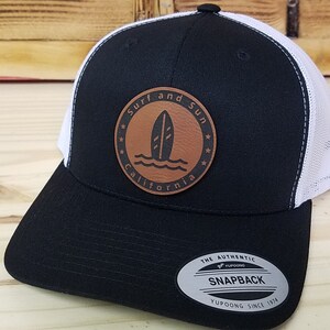 May include: Black and white trucker hat with a brown leather patch that says "Surf and Sun California" with a surfboard graphic.