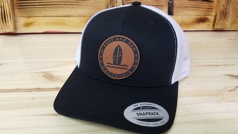 May include: Black and white trucker hat with a brown leather patch that says "Surf and Sun California" with a surfboard graphic.