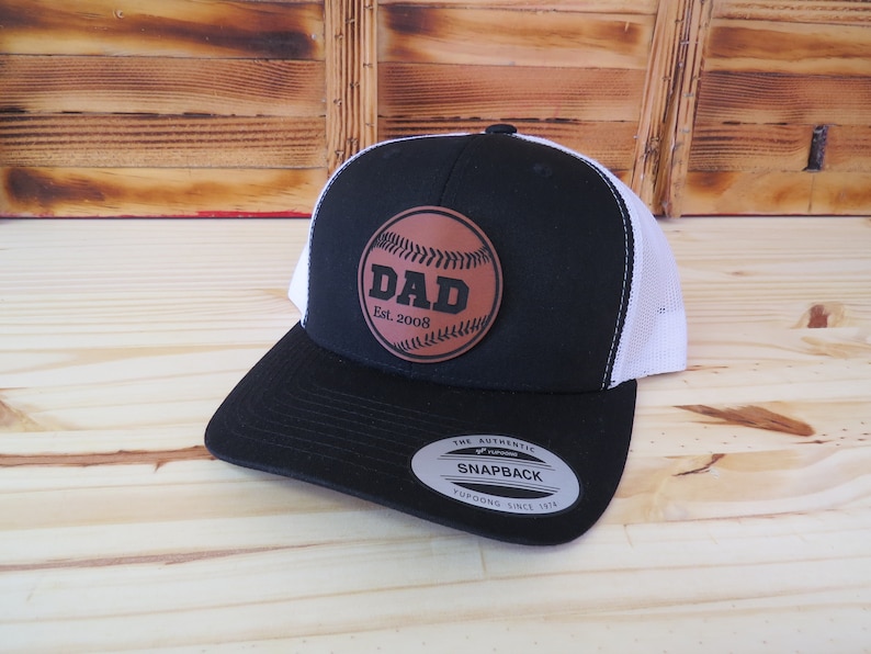 May include: Black and white trucker hat with a brown leather baseball patch that says "DAD Est. 2008".