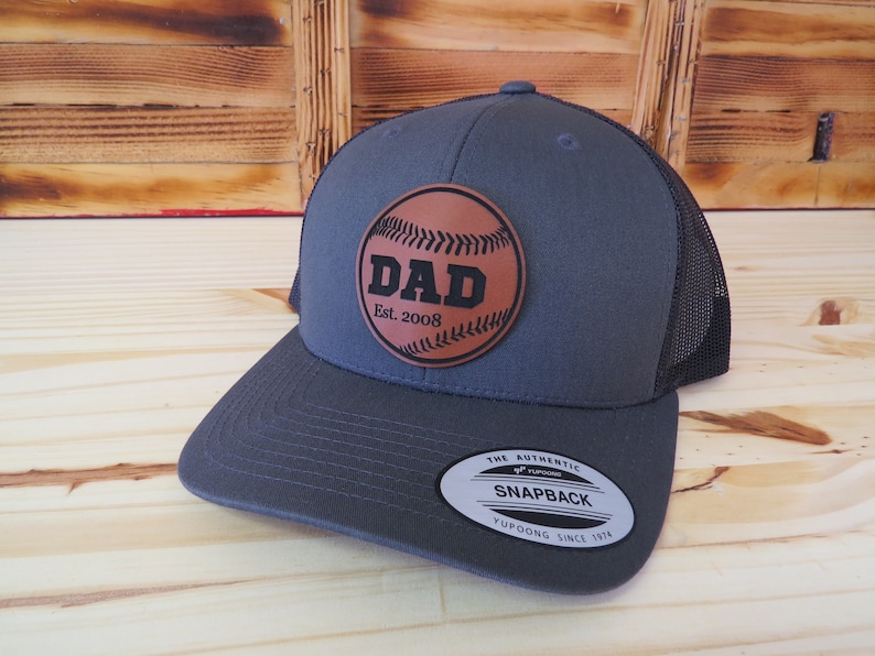 May include: A gray and black baseball cap with a brown leather patch that says "DAD Est. 2008" and a baseball graphic.