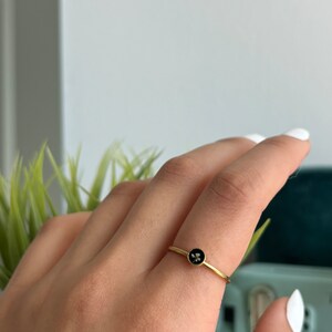 May include: A gold ring with a black circular stone featuring a small flower design.