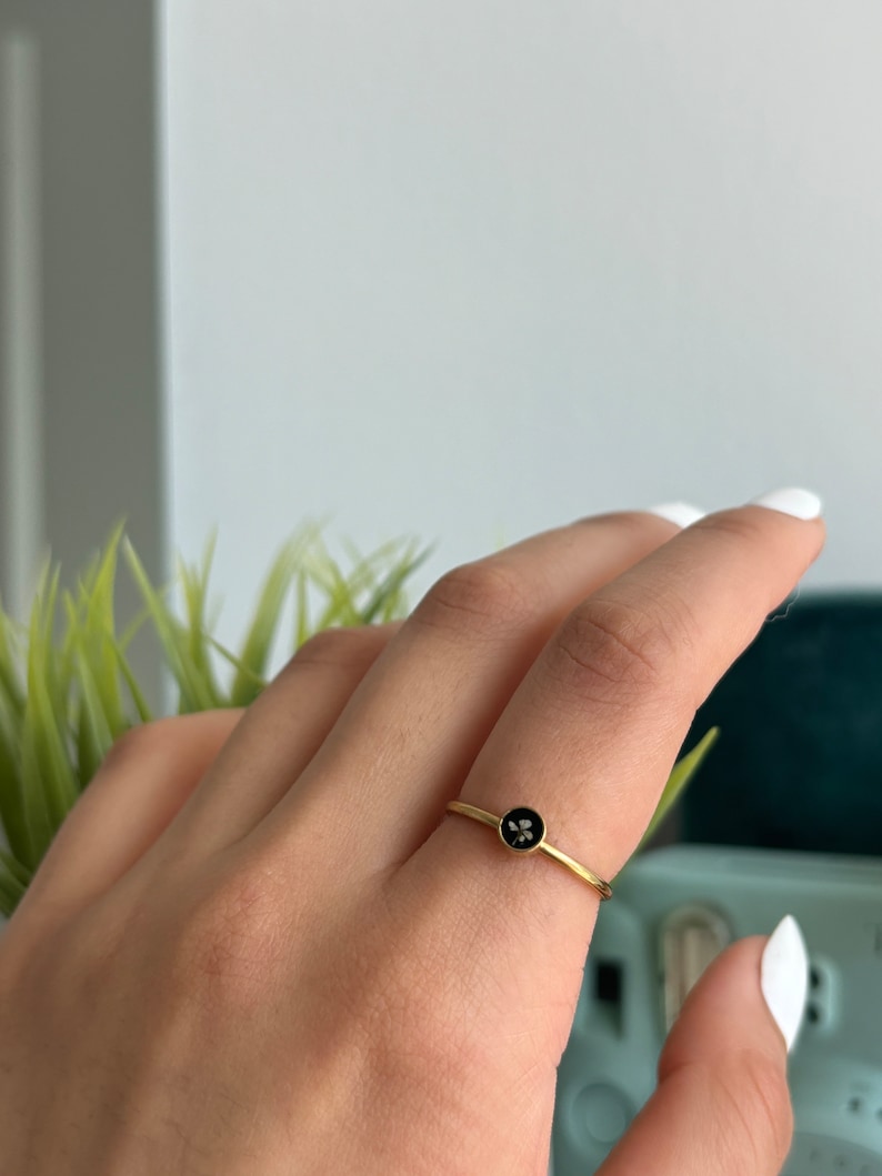 May include: A gold ring with a black circular stone featuring a small flower design.