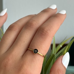 May include: A gold ring with a black round stone featuring a white flower design.