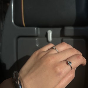 May include: A silver bracelet with a curved design and a silver ring with a small, round, dark gray stone.
