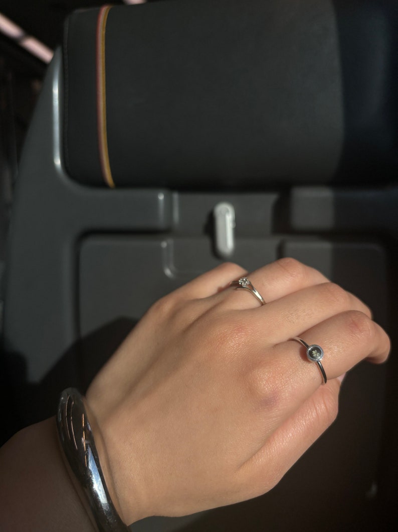 May include: A silver bracelet with a curved design and a silver ring with a small, round, dark gray stone.