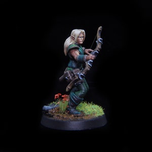 Puede incluir: Una figura en miniatura pintada de un arquero elfo, sosteniendo un arco y una flecha, de pie sobre una base verde con tierra marrón y setas rojas.