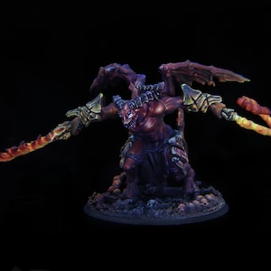 Puede incluir: Una miniatura de demonio rojo y negro con armas naranjas brillantes. El demonio tiene cuernos, alas y una expresión feroz. La miniatura está colocada sobre una base negra con calaveras.