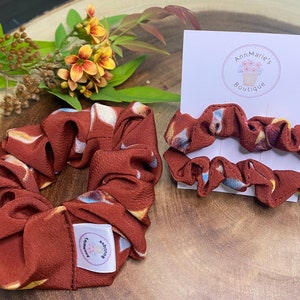 May include: Two brown and white patterned scrunchies. One scrunchie is tied in a knot and the other is laid flat on a white card with the text "AnnMarie's Boutique".