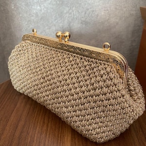 May include: A gold crocheted clutch purse with a gold metal clasp. The purse is made of a fine, delicate yarn and has a classic, elegant design.