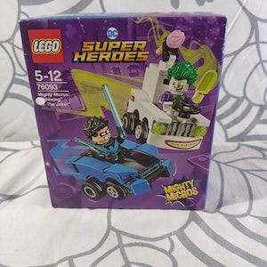 Peut inclure: Un ensemble LEGO DC Super Heroes Mighty Micros avec Nightwing dans un véhicule bleu et le Joker dans une voiture blanche. La boîte est violette avec des accents jaunes et verts et le texte "LEGO", "DC Super Heroes" et "Mighty Micros".