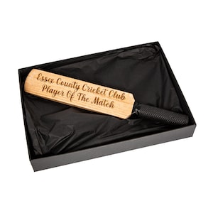 May include: A wooden cricket bat with the text "Essex County Cricket Club Player Of The Match" engraved on the blade. The bat has a black grip and is presented in a black gift box with black tissue paper.
