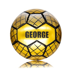 May include: A gold football featuring a black grid pattern and white dot accents on the panels. The name GEORGE is printed in bold black capital letters across the centre panel. The ball has a glossy finish and traditional hexagonal stitching.