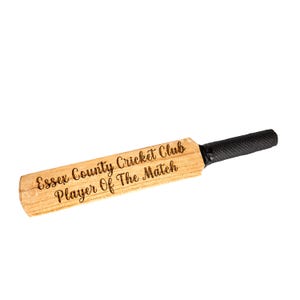 May include: A wooden cricket bat with a black grip. The bat has the text "Essex County Cricket Club Player Of The Match" engraved on the wood.