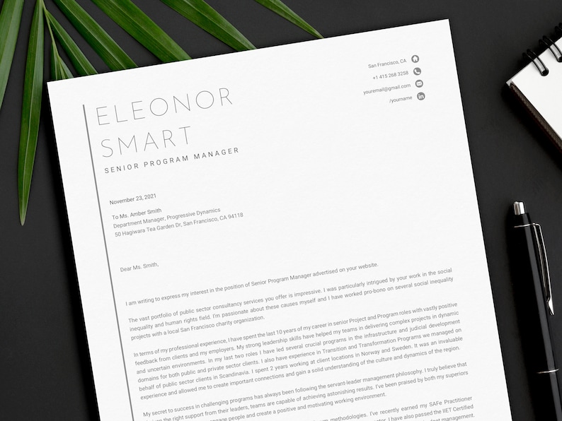 May include: A professional resume on white paper with the name "ELEONOR SMART" and the title "SENIOR PROGRAM MANAGER" at the top. The resume includes contact information, a cover letter, and a black pen on a dark background.