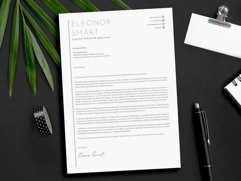 May include: A resume on white paper with the name "Eleonor Smart" at the top. A black pen, a notepad, a binder clip, and a roll of black and white polka dot tape are on a black surface. Green leaves are in the background.