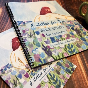 May include: A spiral bound book titled "A Letter for You: Bible Study for Women" by Madeleine Karako. The cover features a watercolor illustration of a person standing in a field of colorful flowers.