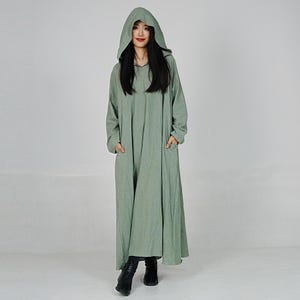 May include: A long, hooded, sage green dress with a relaxed fit and pockets. The dress is made of a soft, comfortable fabric.