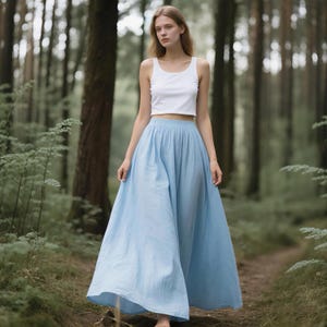 May include: A white sleeveless crop top with a scoop neckline paired with a long, flowing light blue maxi skirt. The skirt features a high-waisted design with a gathered elastic waistband and a full, floor-length silhouette made of solid fabric.