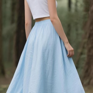 May include: A white sleeveless crop top paired with a long, light blue maxi skirt. The skirt features a gathered elastic waistband and a full, flowing silhouette that reaches the ground, while the top is a simple, fitted sleeveless design.