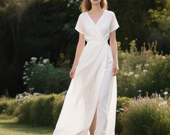 Puede incluir: Un vestido cruzado blanco largo hasta el suelo con mangas cortas, escote en V y una cintura ajustada que se transforma en una falda fluida con una abertura frontal. La prenda está confeccionada con una tela blanca lisa y sencilla.