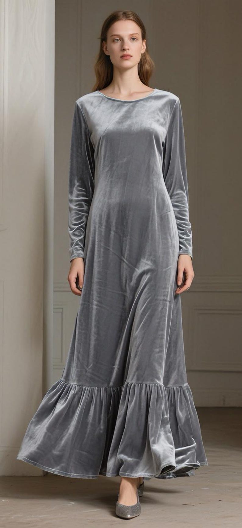 May include: A long, flowing, gray velvet dress with long sleeves and a round neckline. The dress features a ruffled hemline and is floor-length. The fabric has a soft sheen, and the dress appears to be well-tailored.