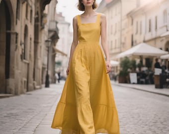 May include: A floor-length mustard yellow sleeveless jumpsuit with a square neckline and wide-leg trousers. The garment features a fitted bodice, a defined waistline, and a tiered skirt-like overlay that creates a flowing silhouette while walking.