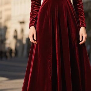 May include: A long, burgundy velvet dress with long sleeves. The dress has a fitted bodice and a flowing skirt. The sleeves are ruched at the wrists. The dress is suitable for formal occasions.