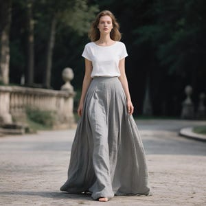 Op de afbeelding: Een vrouw draagt een witte top met korte mouwen en een lange, grijze rok. De rok heeft een hoge taille en een wijd, geplooid ontwerp. De outfit is geschikt voor casual of formele gelegenheden.