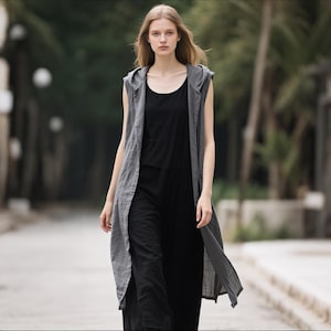 Puede incluir: Un chaleco sin mangas con capucha en color gris carbón, de largo hasta la rodilla, sobre una camiseta negra de cuello redondo y pantalones negros a juego. El chaleco presenta un diseño abierto en la parte frontal y una capucha.