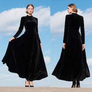 May include: A full-length black velvet dress featuring a high neckline and long sleeves. The dress has a flowing skirt and is paired with black heels. The backdrop is a blue sky with clouds. The dress exudes elegance and formality.