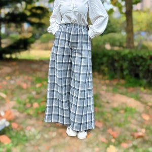 May include: Wide-leg plaid pants in shades of gray, white, and blue. The pants have a high waist and are paired with a white button-down shirt. The pants are made of a soft, woven fabric.