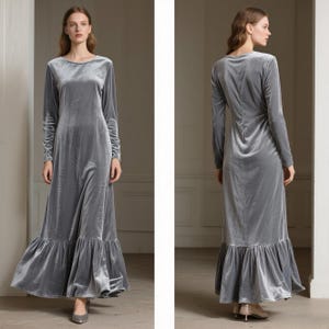 May include: A long, gray velvet dress with long sleeves and a ruffled hem. The dress has a round neckline and a flowing silhouette. The fabric has a soft, lustrous appearance. The dress is suitable for formal occasions.