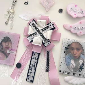 May include: A decorative rosette made of pink satin ribbons, white ribbons with black polka dots, and black ribbons with white musical notes, accented with white lace. Includes two photo holders, two plush wing clips with beads, and a beaded keychain.