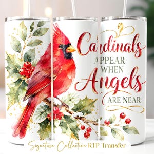 May include: A cylindrical white tumbler featuring a watercolor illustration of a bright red cardinal perched on a holly branch with green leaves and red berries. The text reads Cardinals APPEAR WHEN Angels ARE NEAR in red and black script.