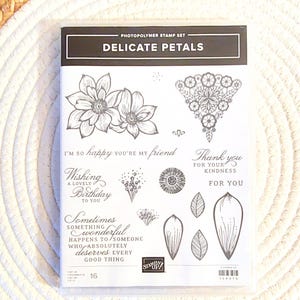 May include: A white ceramic mug with a black handle and the text "But First, Coffee" in a bold, black font. The mug is set against a blurred background, suggesting a cozy setting.