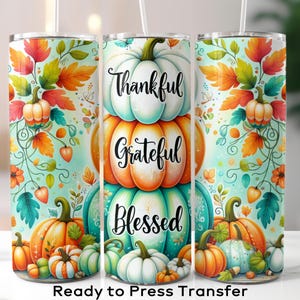 May include: A set of three stainless steel tumblers with a fall-themed design. The design features stacked pumpkins in white, orange, and teal, with the words "Thankful, Grateful, Blessed." The tumblers are decorated with autumn leaves and pumpkins.