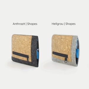 Puede incluir: Dos carteras de corcho y fieltro, una en gris oscuro y otra en gris claro, con cierre de cremallera y el texto "Anthrazit | Shapes" y "Hellgrau | Shapes" encima de cada una.