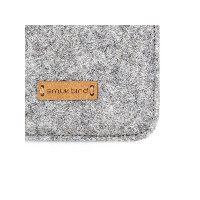 May include: Close-up of a gray felt pouch with a brown leather label that reads "smukbird".